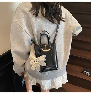 Detail of a black glossy bucket bag with a white flower charm worn by a model