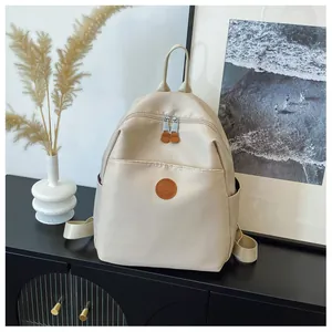 Detail view of beige nylon backpack with leather zipper pull and round logo badge