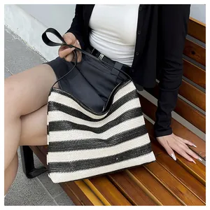 Détail d'un sac de plage tressé à rayures noires et blanches porté par un mannequin assis