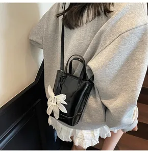 Detail of black glossy mini bucket bag featuring a large white fabric flower charm
