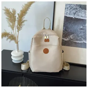 Close-up of cream nylon backpack with leather logo patch and dual zipper design