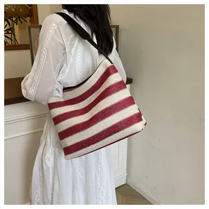 Détail du sac de plage en paille à rayures rouges et blanches avec bandoulière noire sur modèle