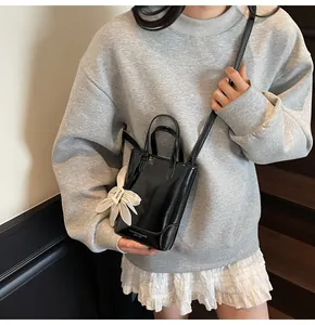 Close-up of a glossy black patent leather bucket bag with a white flower charm and strap