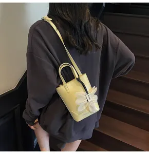 Detail of light yellow bucket bag with floral motif and adjustable strap on a model