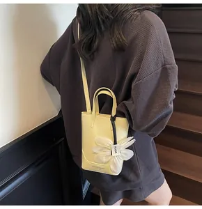 Detail of yellow bucket bag featuring a white flower charm and embossed leather logo