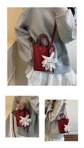 Detail view of red mini bucket bag with a large white mesh flower charm and printed text