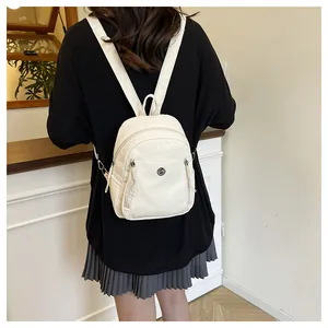 Detailansicht eines weißen Rucksacks mit GM-Metalllogo, getragen von einem Modell in Innenraum