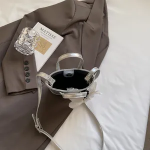Minimalist silver bucket bag with double handles and a white flower charm on a blazer