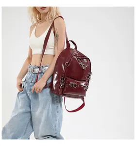 Détail du sac à dos verni bordeaux avec pendentif croix punk et anneaux métalliques