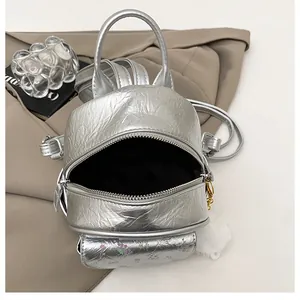 Detail of silver mini backpack with floral front pocket and plush white pompom charm