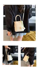 Detail of beige mini bucket bag with tulip charm and crossbody strap in a warm setting