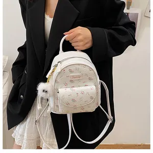 Detail of white mini backpack with floral pattern, metal logo, and plush monster charm