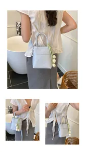 Detail view of light blue leather bucket bag featuring a tulip charm and green ribbon strap