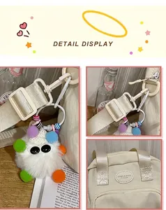 Detail showing cream canvas crossbody bag with fluffy monster charm and logo patch