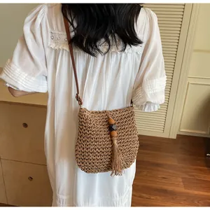 Detail of hand-woven straw crossbody bag with decorative tassels and leather strap