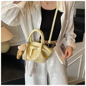 Detail of light yellow crocodile texture handbag with decorative strap and bear charm