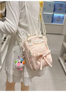 Detail of light pink canvas crossbody bag with bow decoration and fluffy white charm
