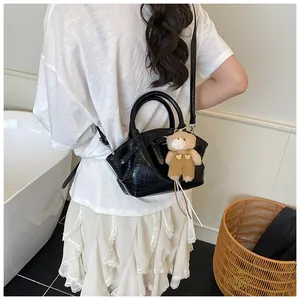 Detail of black crocodile texture handbag with a cute brown plush bear charm and strap