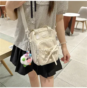 Detail of beige nylon crossbody bag with bow design and colorful plush pompom charm