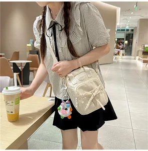 Chic beige crossbody bag with bow detail and fuzzy monster charm in a lifestyle setting