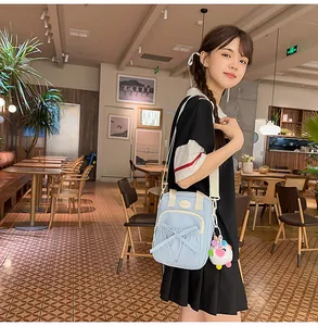 Detail of light blue canvas crossbody bag with bow design and colorful plush ball