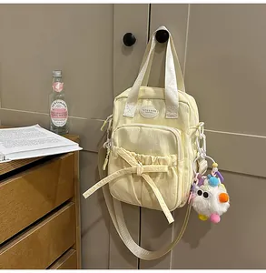 Detail of light yellow canvas handbag with decorative bow and plush ball charm hanging