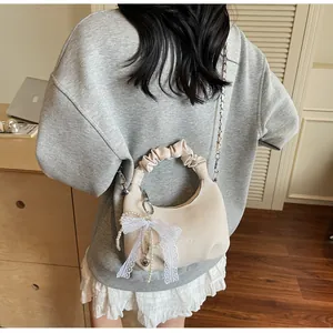 Détail du sac coquillage crème avec nœud en dentelle et breloque perle sur le modèle