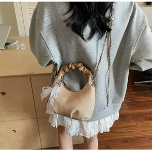 Détail d'un sac à bandoulière beige avec poignée plissée, nœud en dentelle et perles