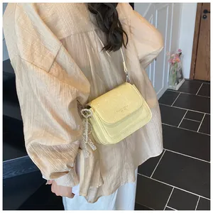 Detail of light yellow crossbody bag with litchi texture and pearl lace pendant