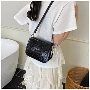 Detail of black glossy patent leather crossbody bag with pearl charm and fashion logo