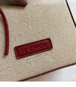 Detail of cream canvas bag with deep red leather trim and IT CHICK embossed logo label
