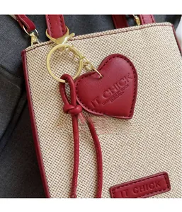 Close-up of beige woven handbag with red leather trim and a heart-shaped charm detail