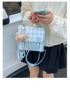 Detail of blue plaid mini backpack with plush bear charm and pink ribbon decoration