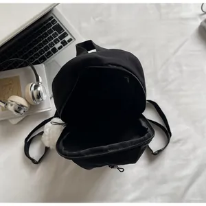 Vista interna del mini zaino nero con tasca a zip, ciondolo a pompon e fodera interna