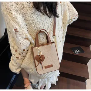 Detail of beige canvas crossbody bag with brown leather trim and heart charm