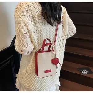 Detail of a beige canvas and red leather mini bag with IT CHICK logo and heart charm