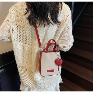 Detail of mini canvas crossbody bag with red leather trim and heart logo charm