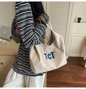Detail of embroidered letters on off-white canvas tote with brown leather handle