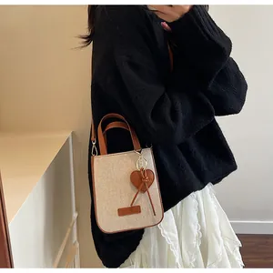 Close-up of stylish beige denim crossbody bag with brown leather trim and heart charm