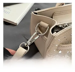 Detailed close-up of a premium metal hook and rhinestone decor on a beige saddle bag