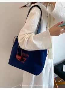 Detail view of navy canvas tote with red cursive embroidery and mini leather pouch