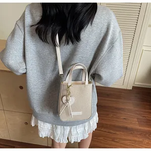 Detail of small beige woven tote bag with leather trim and a heart charm pendant
