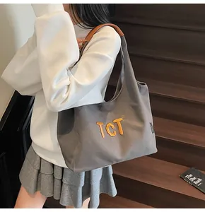 Macro detail of embroidered TCT letters and brown leather handles on grey canvas tote