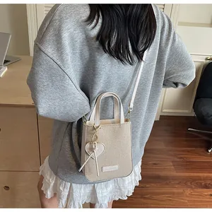 Detail of a beige canvas bucket bag featuring heart leather charm and thin shoulder strap