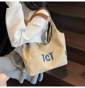 Detail view of large canvas tote bag with brown leather handles and blue TCT embroidery