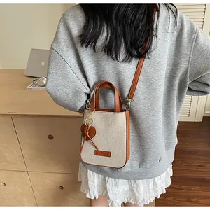 Detail of canvas crossbody bag with heart charm shown on model in cozy indoor setting