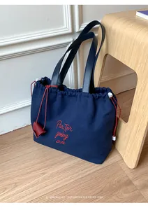 Detailed close-up of blue canvas tote bag with red embroidery and leather handles
