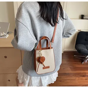 Detail of canvas and brown leather crossbody bag with heart charm and IT CHICK label