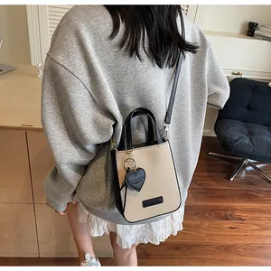 Chic beige woven mini bag with black leather trim and IT CHICK heart charm shown on model