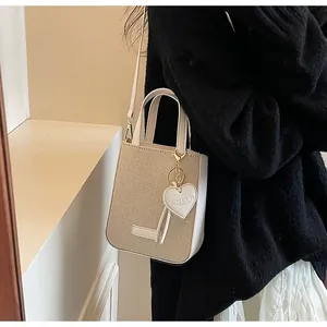 Detail of beige woven tote with leather trim, heart charm, and adjustable crossbody strap